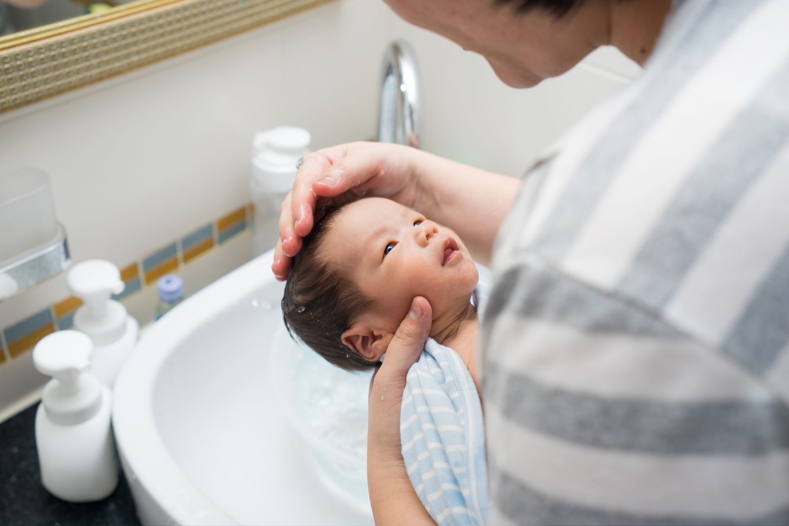 A caregiver gives a newborn a bath in a small sink