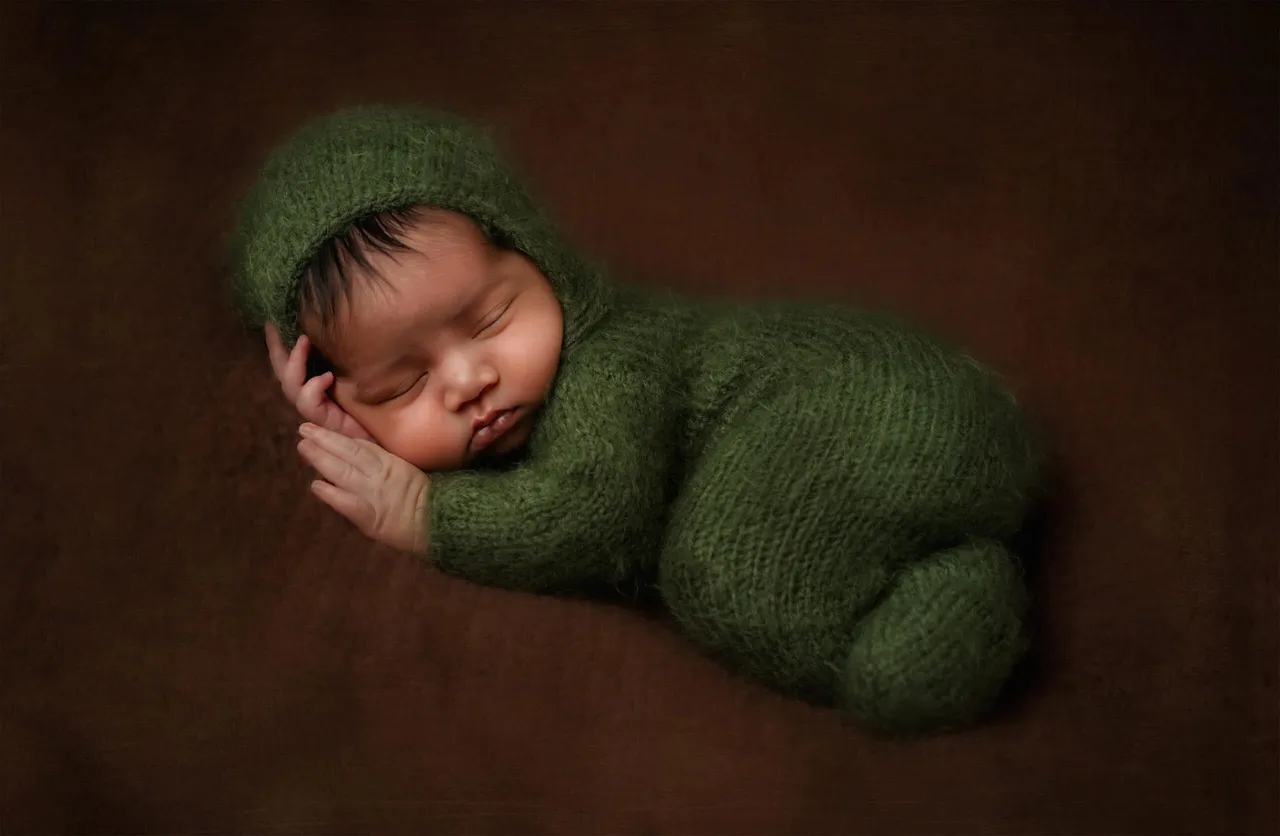 A sleeping newborn in a green knit outfit
