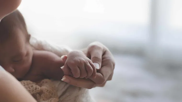 A caregiver's hand holding a sleeping newborn's hand