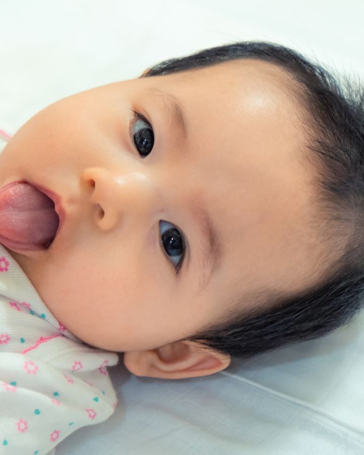 A baby lies on a blanket and sticks out their tongue