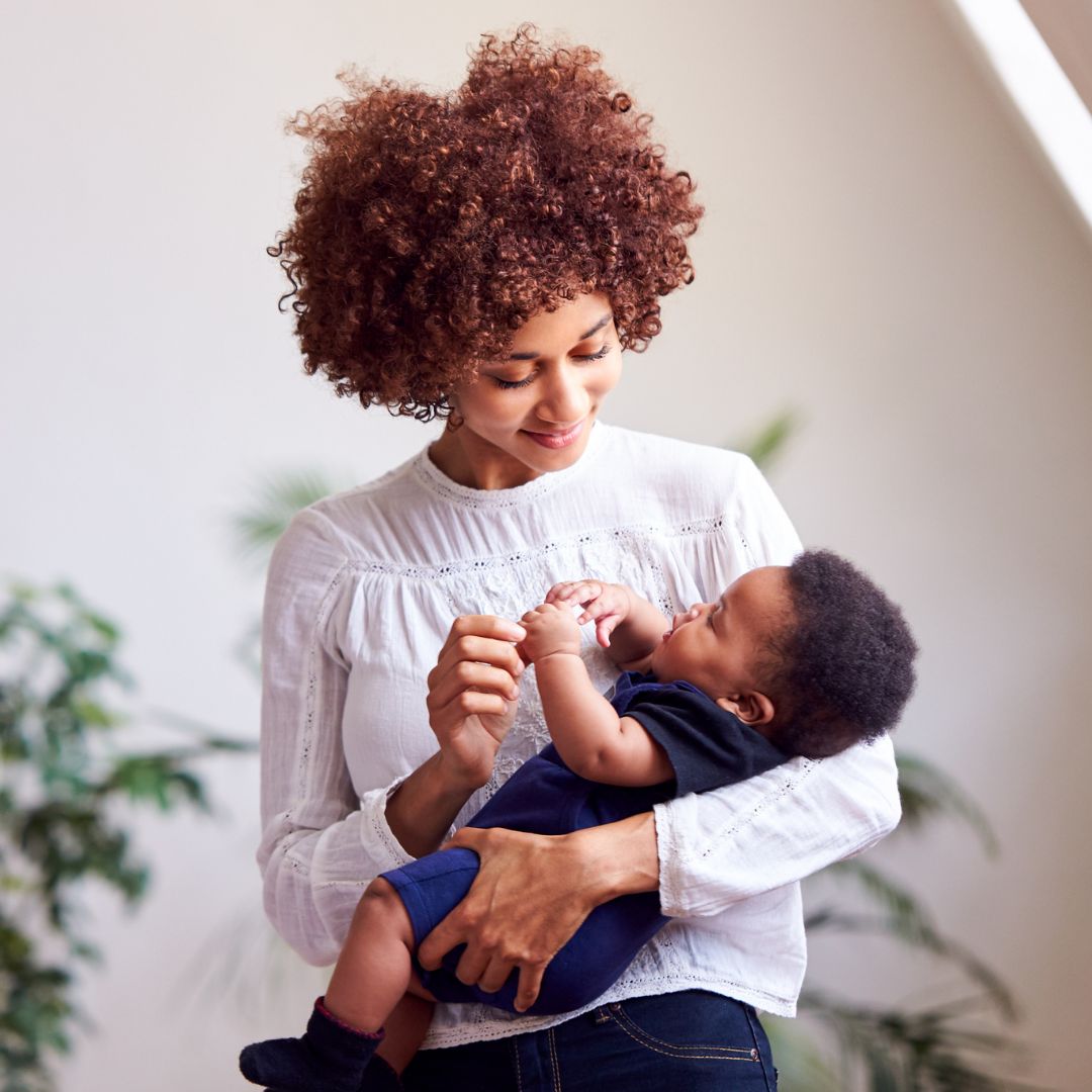 A smiling caregiver holds a baby in a bright room