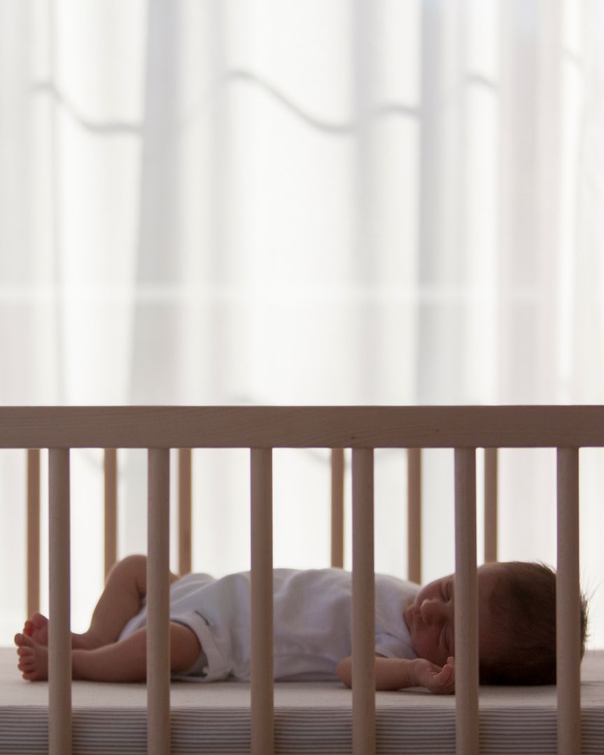A newborn sleeps in a crib by a sunny window