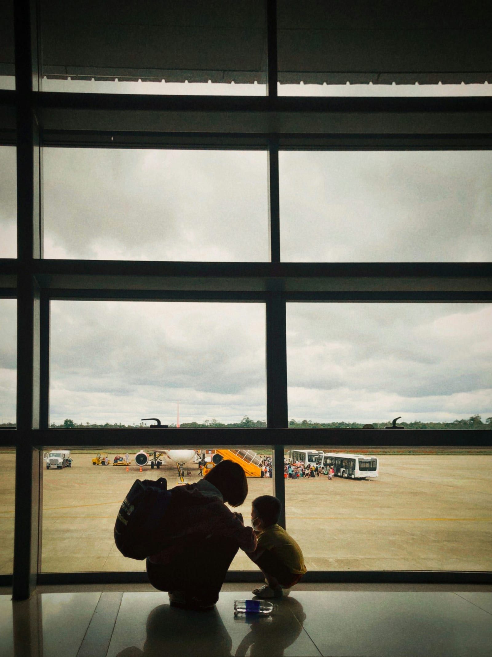 A caregiver and child look out at planes through an airport window